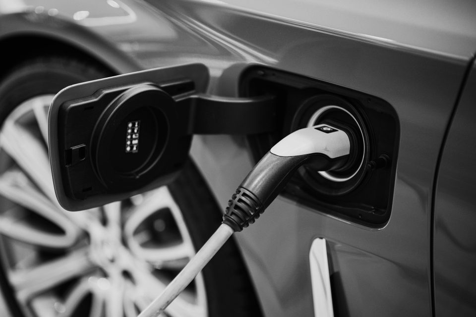 Svartvit bild av en elbil som laddas med hjälp av solceller och en laddbox. Bilden illustrerar användningen av förnybar solenergi för att driva elfordon och främja hållbar mobilitet.