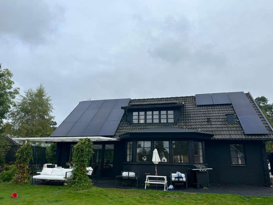 En bild av en svart villa med solceller på taket. Solcellerna är svarta och smälter väl in med takets färg. De absorberar solens strålar och omvandlar dem till elektrisk energi. Solcellerna bidrar till att förse huset med förnybar energi och minskar beroendet av traditionella energikällor. Detta ger en hållbar och miljövänlig lösning för energiproduktion.