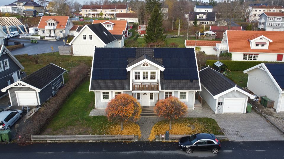 Bild på solceller installerade av Solifokus på ett tak i Jönköping. På bilden syns huset med solceller samt en laddbox för elbilar. Bilden är tagen från en höjd och ger en tydlig framifrån vy av installationen