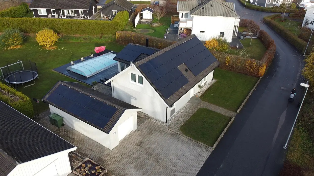 En villa med solceller på taket och en pool i trädgården där solcellerna har installerats av Solifokus och kombinerar hållbar energiproduktion med en avkopplande utomhusmiljö